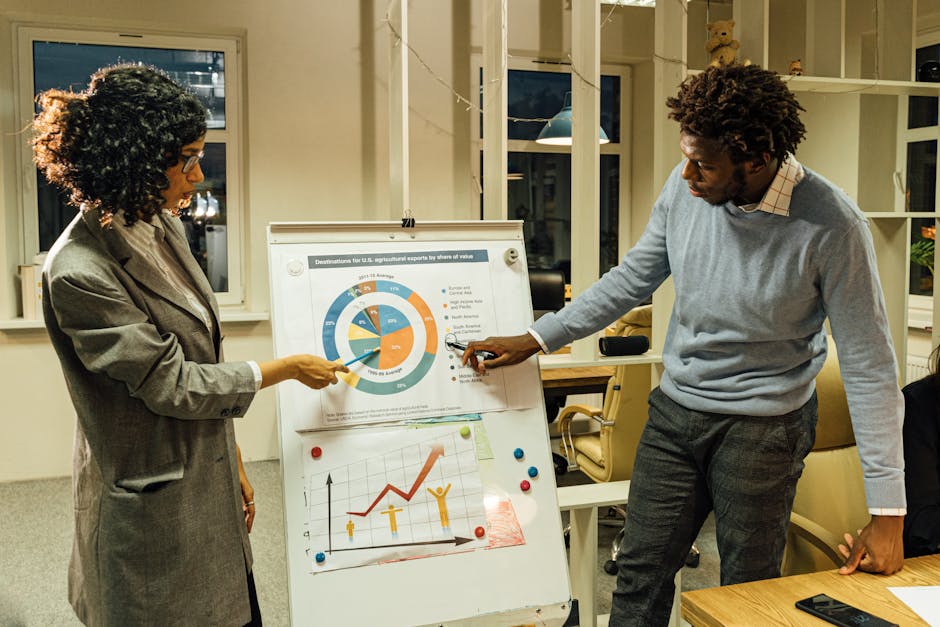 Two professionals engaged in a business meeting discussing charts on a whiteboard in a modern office.